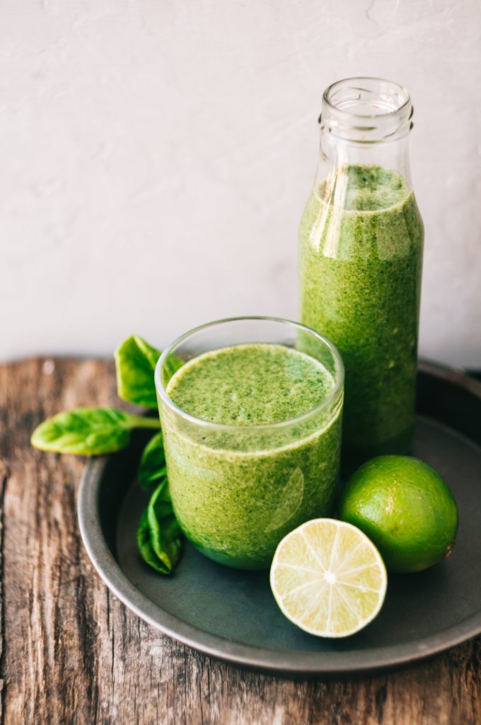 a glass with a green drink and limes on a table