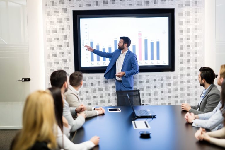 a person standing in front of a screen with people sitting around it