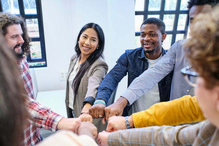 coworkers in casual clothes smiling and looking at each other while bumping fists in office